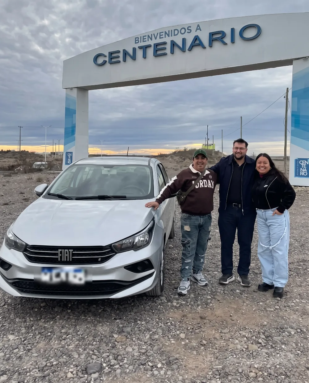 Entrega de un Fiat Cronos gris en Centenario, Neuquén, bajo el arco de bienvenida de la ciudad